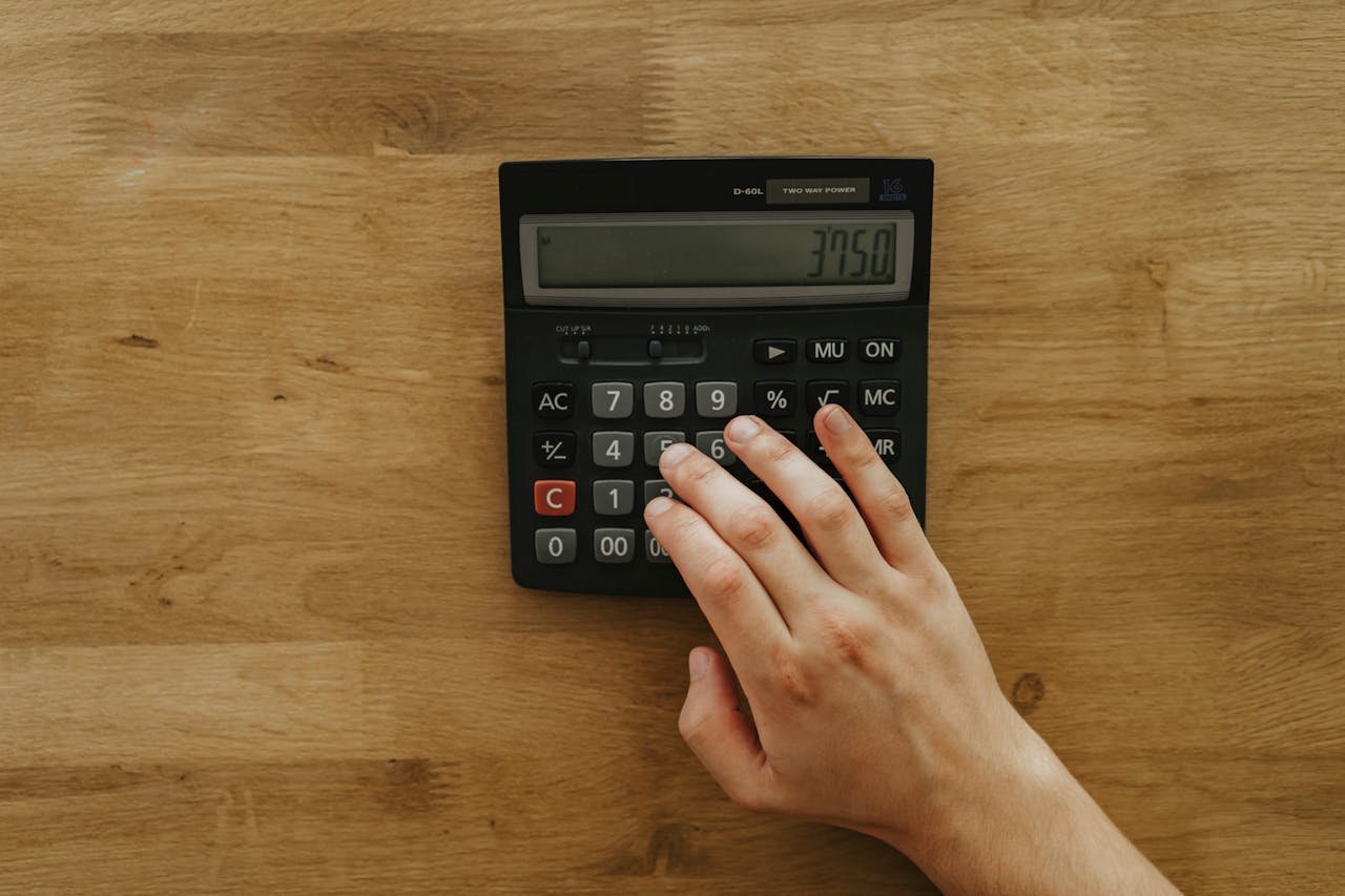 services-04 A person's hand pressing keys on a calculator displaying 3750 on a wooden table, top view.